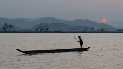 Le soir venu dans une atmosphère brumeuse, un pêcheur manie sa barque sur le lac