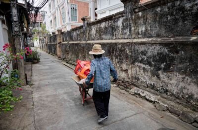 Homme poussant une brouette portant des tabourets en plastique dans une ruelle étroite avec mur ancien