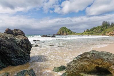 Plage tropicale où émergent des rochers et plus loin, de la végétations sur des collines